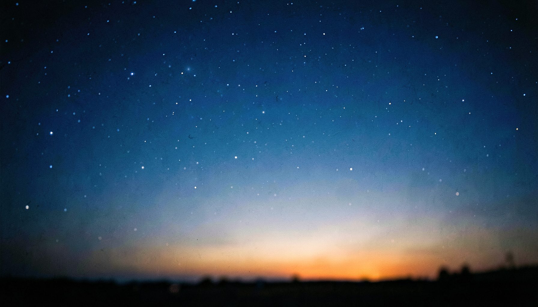 Deep blue night sky with scattered stars fading into a warm horizon glow, wide cinematic frame with shallow depth of field