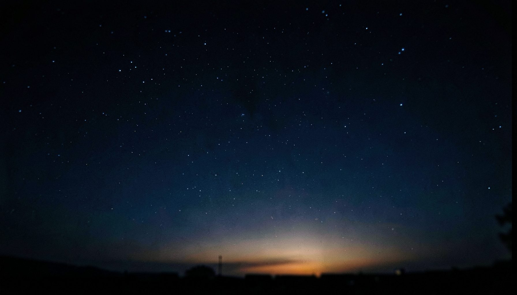 Dark navy night sky with scattered stars and a subtle warm glow near the horizon, deep blue and black tones