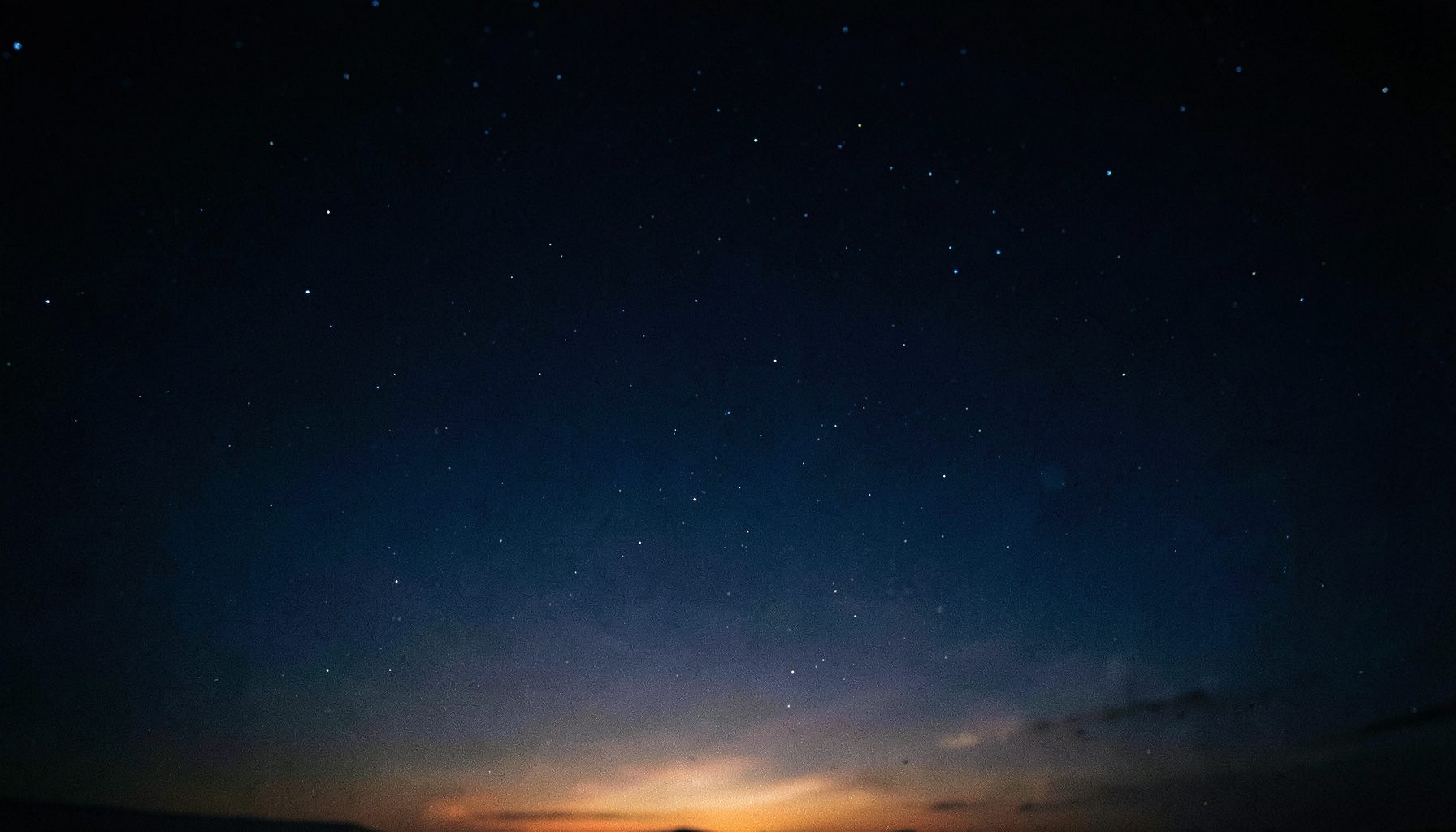 Dark navy night sky with scattered soft stars and a subtle warm glow near the horizon, deep blue and indigo tones