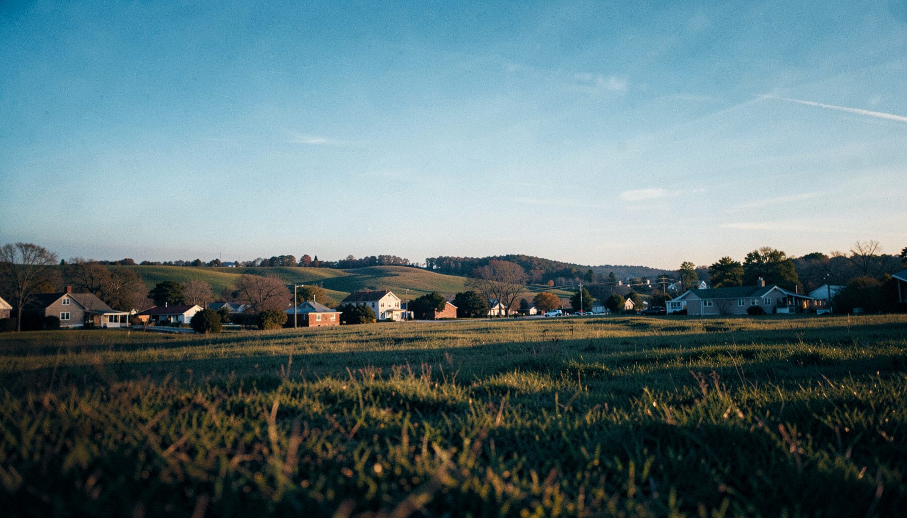 Wide landscape view of a Midwestern community in Lorain County under a soft blue sky, with gentle rolling fields and modest town buildings